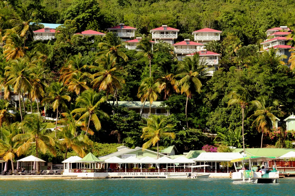 Waterfront restaurant and a small boat on Marigot Bay, Saint Lucia, with palm trees and hillside villas behind
