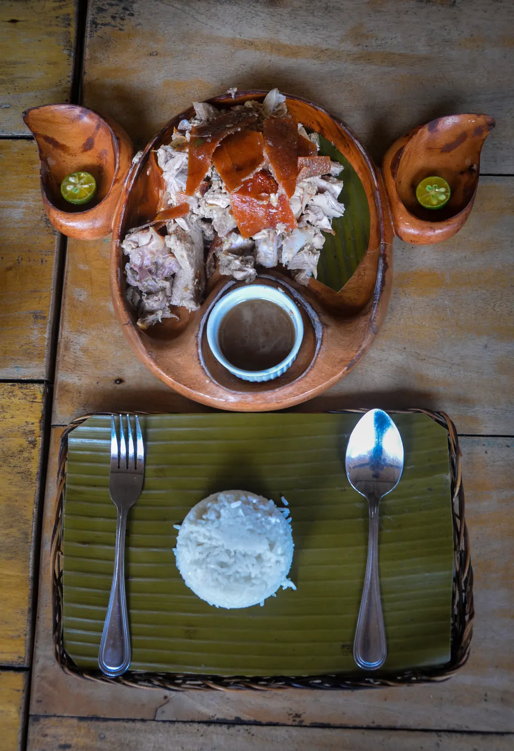 A plate of Cebu lechon with crisp skin, a cup of sauce, calamansi and a mound of rice on a banana leaf
