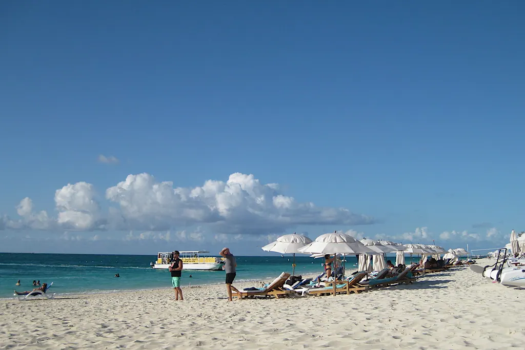White sand, beach umbrellas and loungers on Grace Bay, Providenciales, with a tour boat on turquoise water