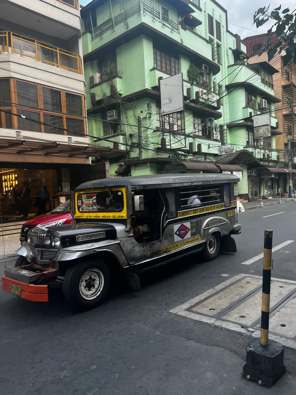 A silver jeepney with yellow and red trim driving down a quiet street in Metro Manila