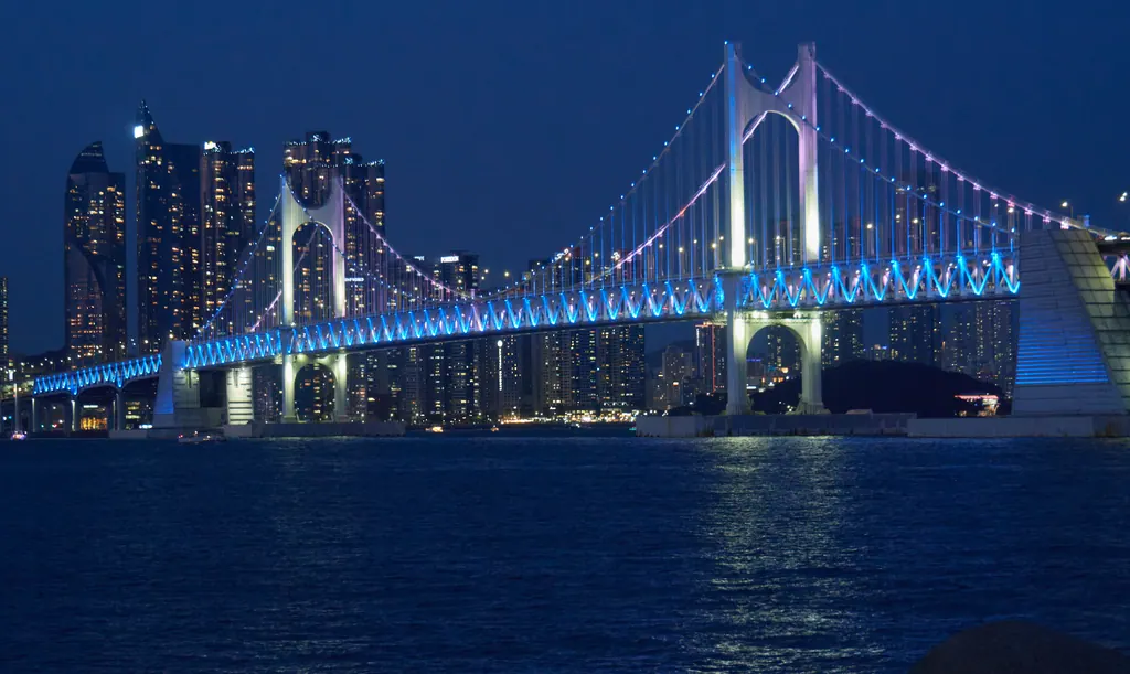 Gwangan Bridge lit in blue at night over the bay at Gwangalli Beach in Busan, with high-rise towers behind