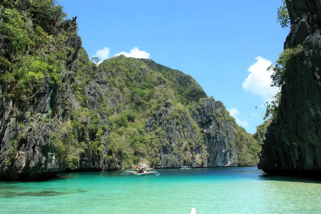 An outrigger boat in the turquoise water of the Big Lagoon at El Nido, surrounded by limestone cliffs