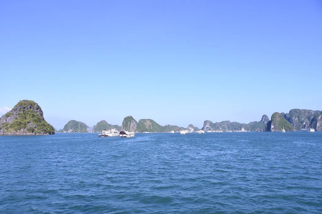 Limestone karst islands and tour boats on the blue water of Ha Long Bay under a clear sky