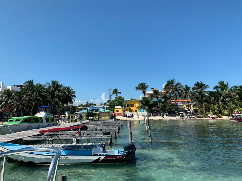 Water taxis and small boats moored at a wooden dock on Caye Caulker, with palm trees and beachfront buildings behind