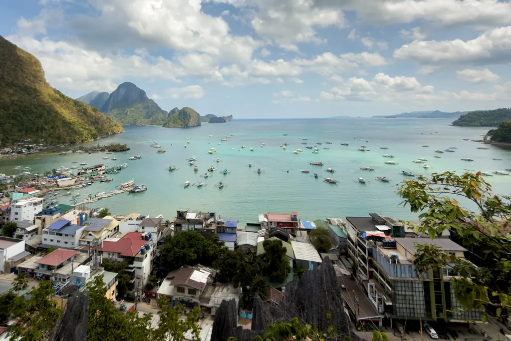 Outrigger bangka boats scattered across the turquoise water of Bacuit Bay off El Nido town, with limestone islands on the horizon