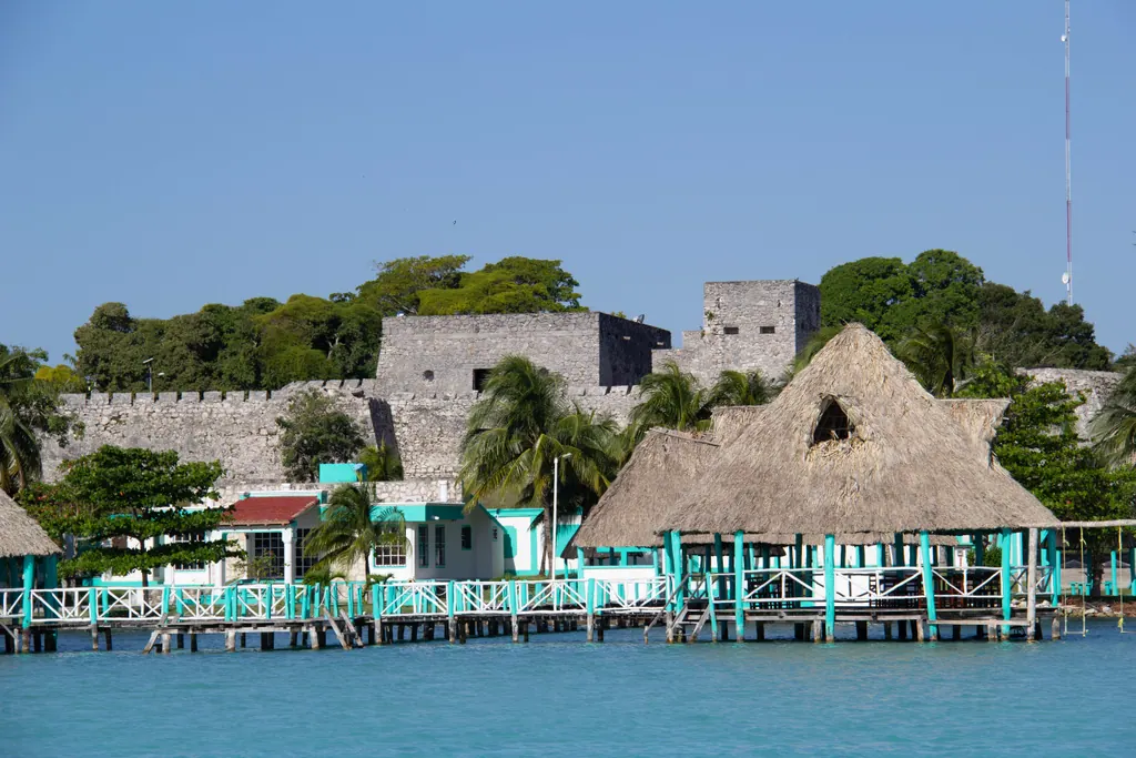 The lagoon at Bacalar with a wooden pier, a palm-roofed building and the old stone fort behind