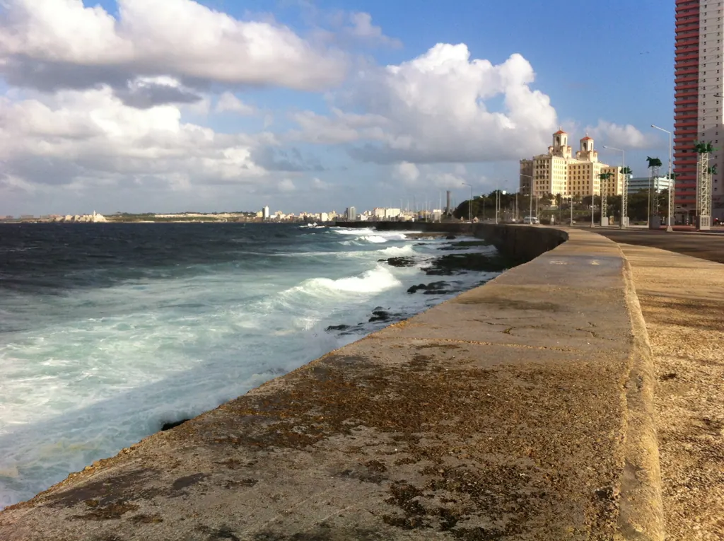 Waves breaking against the long seawall of the Malecon in Havana on a sunny day with clouds