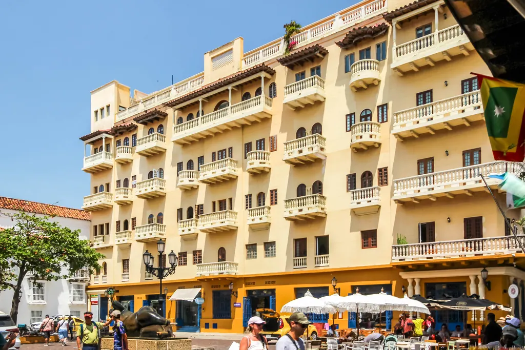 Outdoor restaurant tables and umbrellas below a yellow colonial building on Plaza de Santo Domingo in Cartagena, Colombia