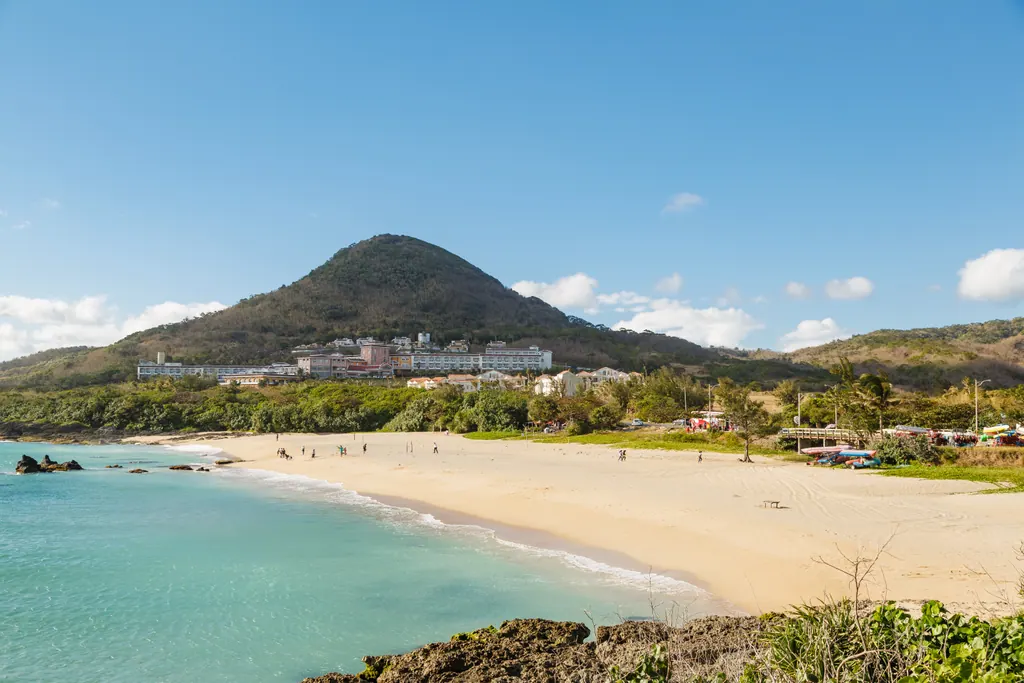 A sandy beach with turquoise water and a green hill behind it in Kenting
