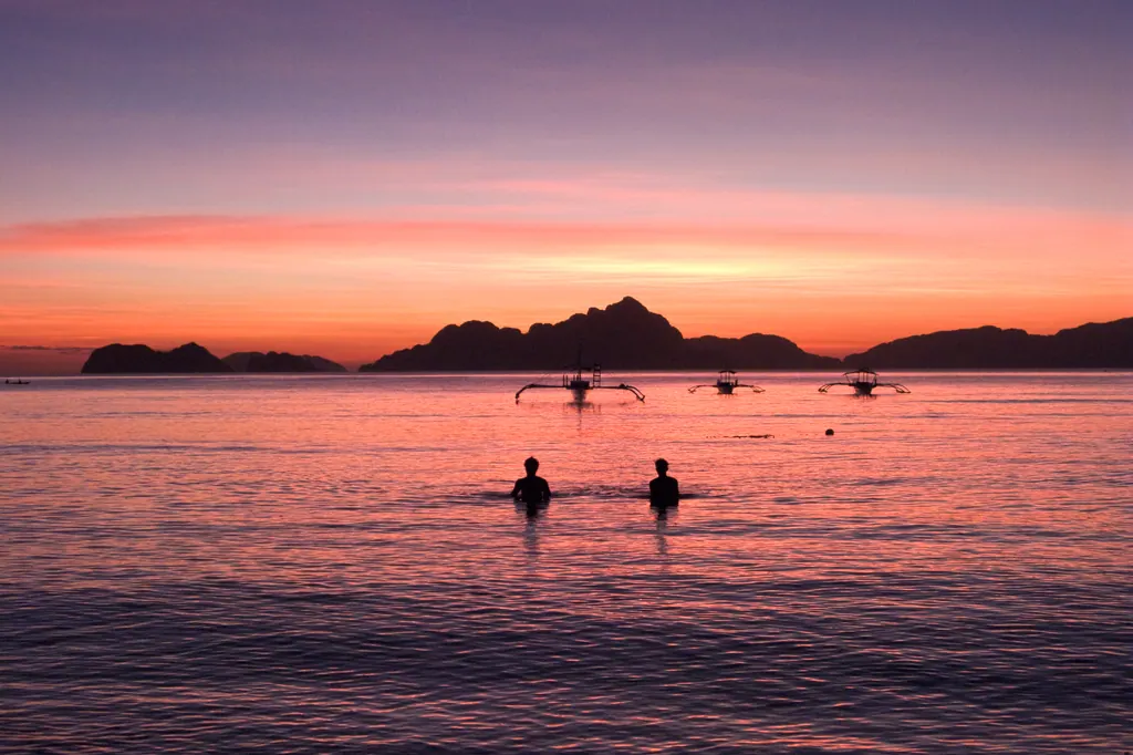 Sunset over Bacuit Bay in El Nido, with outrigger boats and limestone islands on the horizon