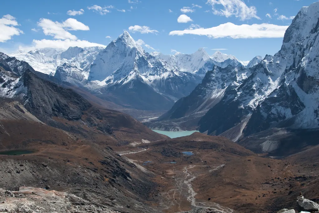 The pointed summit of Ama Dablam and snowy Himalayan peaks above a high valley with a glacial lake in the Everest region