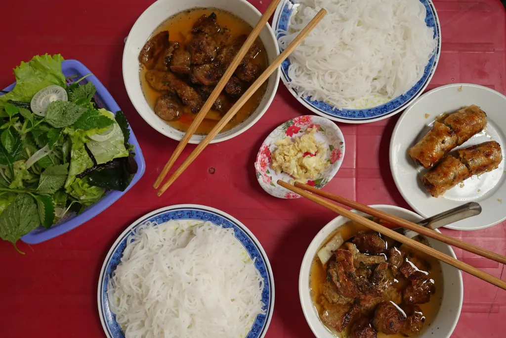 Bun cha with grilled pork in dipping broth, rice noodles, fresh herbs and fried spring rolls on a red table in Hanoi