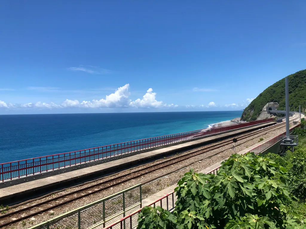 Railway tracks and platforms at Duoliang Station running along a green hillside above the blue Pacific Ocean on Taiwan's east coast