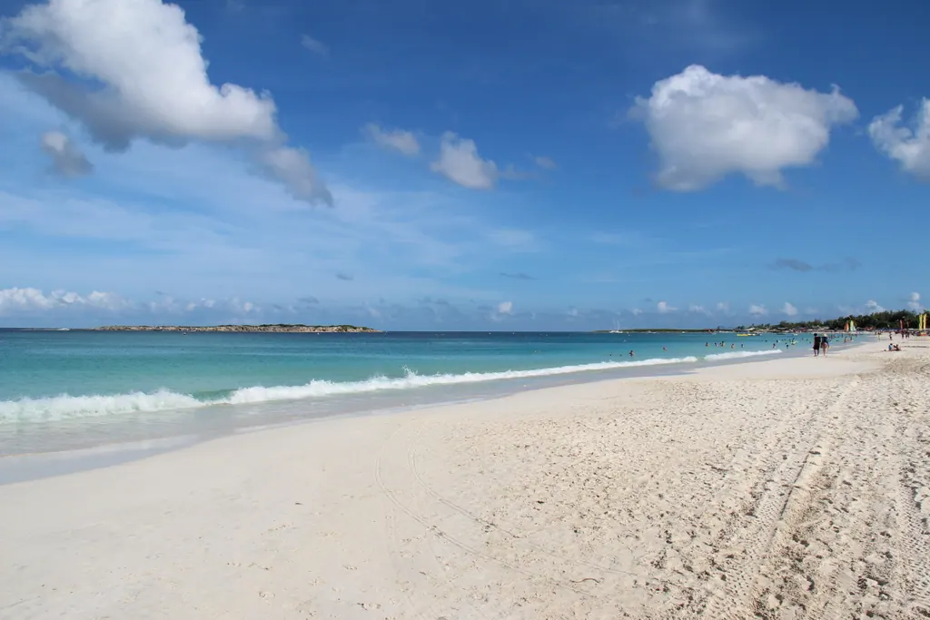 Wide white sand beach at Orient Bay on Saint Martin with turquoise water and small islands on the horizon