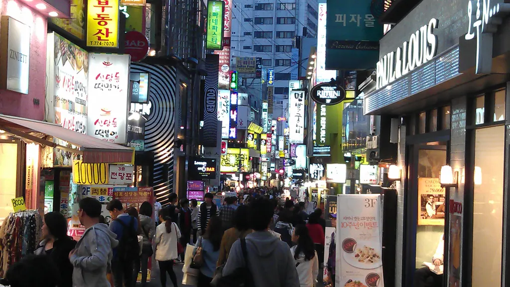 Shoppers walking along a Myeongdong shopping street in Seoul at night under illuminated shop signs