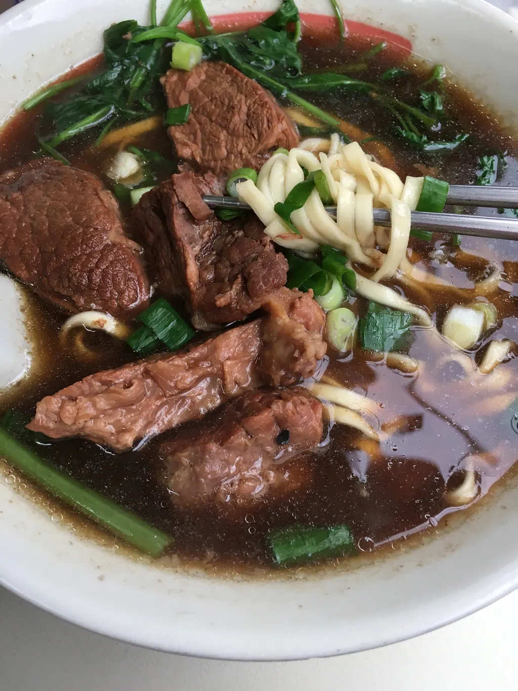 A bowl of Taiwanese beef noodle soup with braised beef and greens