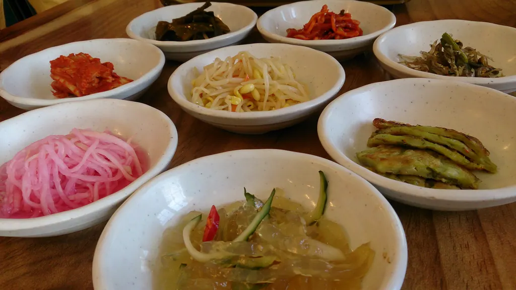 A spread of Korean banchan side dishes in white bowls on a wooden table