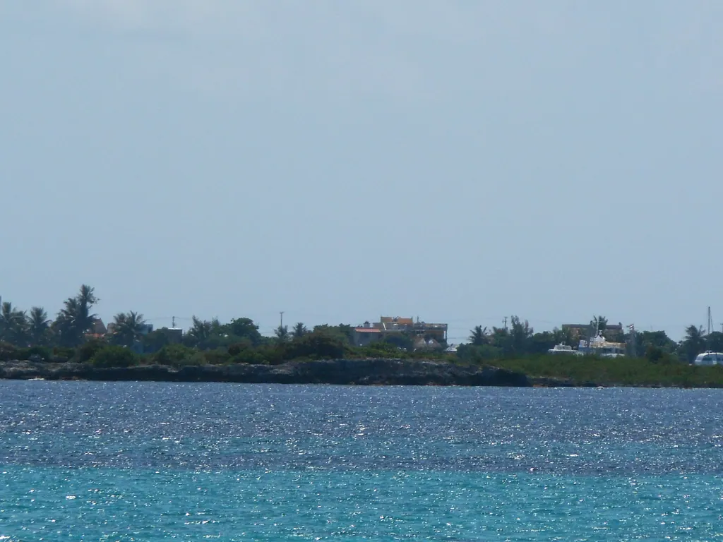 The low green coast of Isla Mujeres seen across turquoise water from the ferry