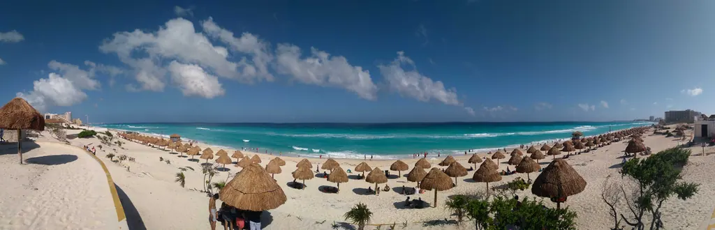 Wide sandy beach with palapa umbrellas and turquoise surf at Playa Delfines in Cancún
