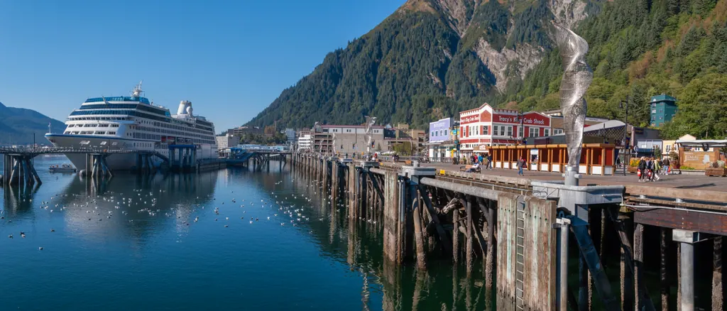 Wide view of Juneau, Alaska, with a cruise ship docked by the waterfront and forested mountains behind