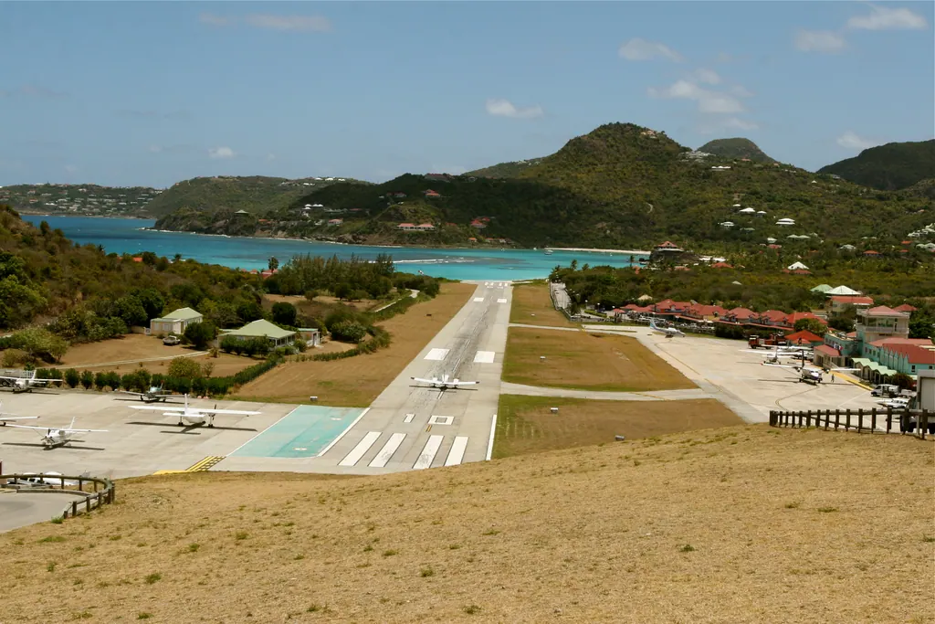 The short runway of Gustaf III Airport on Saint Barts seen from the hill, with small planes parked and Saint-Jean Bay behind