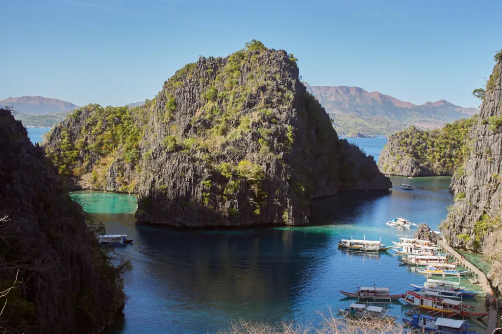 Wooden outrigger bangkas moored at a jetty below steep limestone cliffs and turquoise water on Coron Island