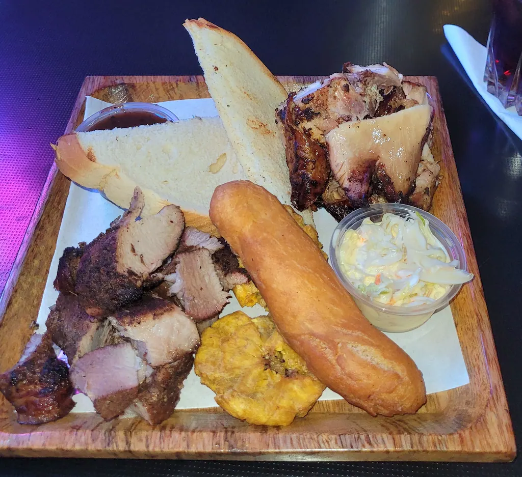 A plate of Jamaican jerk pork and chicken with hard dough bread, festival, fried plantain and coleslaw