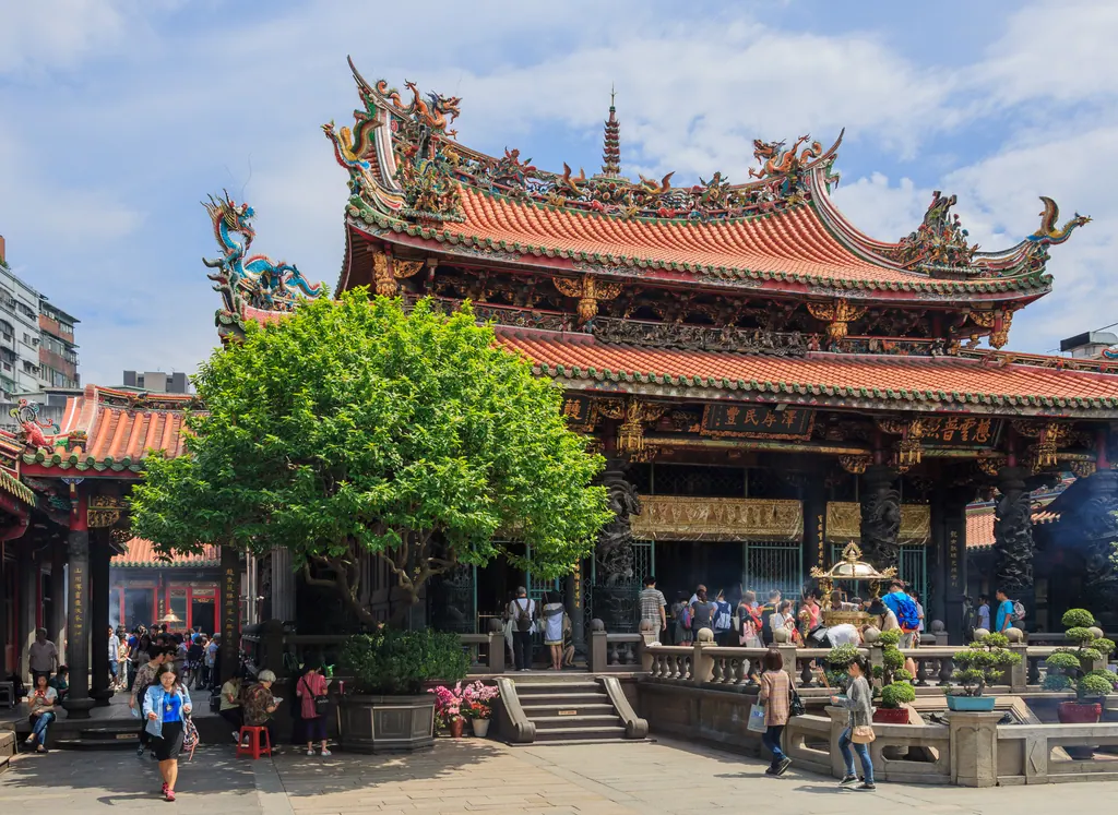 The ornate main hall of Mengjia Longshan Temple in Taipei with curved tiled roofs and dragon decorations under a blue sky