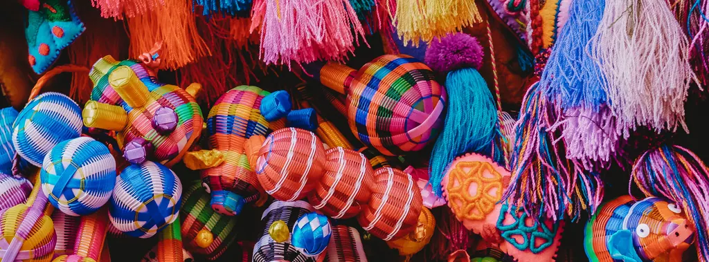 Brightly colored woven Mexican craft toys with tassels piled closely together