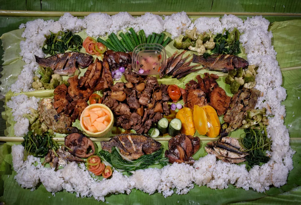 A kamayan feast laid out on banana leaves, with grilled fish, pork and vegetables framed by a border of white rice