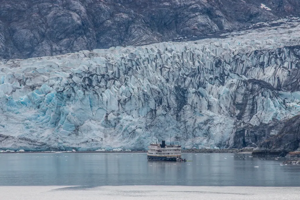A small cruise ship in front of a towering blue and white tidewater glacier in Glacier Bay, Alaska